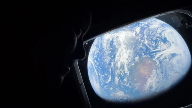 Reid Wiseman peers out of one of the Orion spacecraft's main cabin windows, looking back at Earth.
